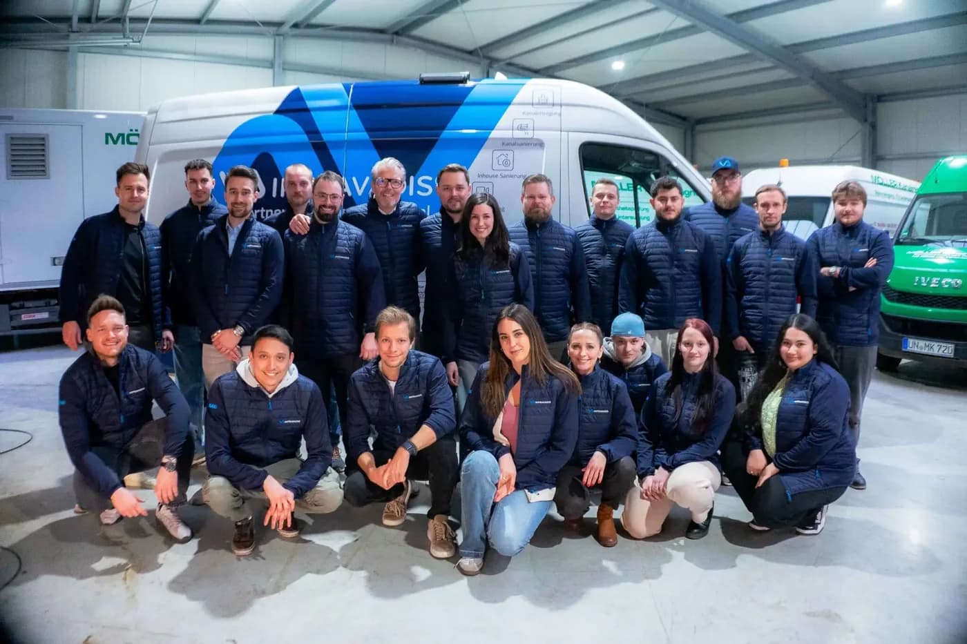 Das Team von Infravadis in Firmenjacken vor einem beschrifteten Servicefahrzeug in der Fahrzeughalle.